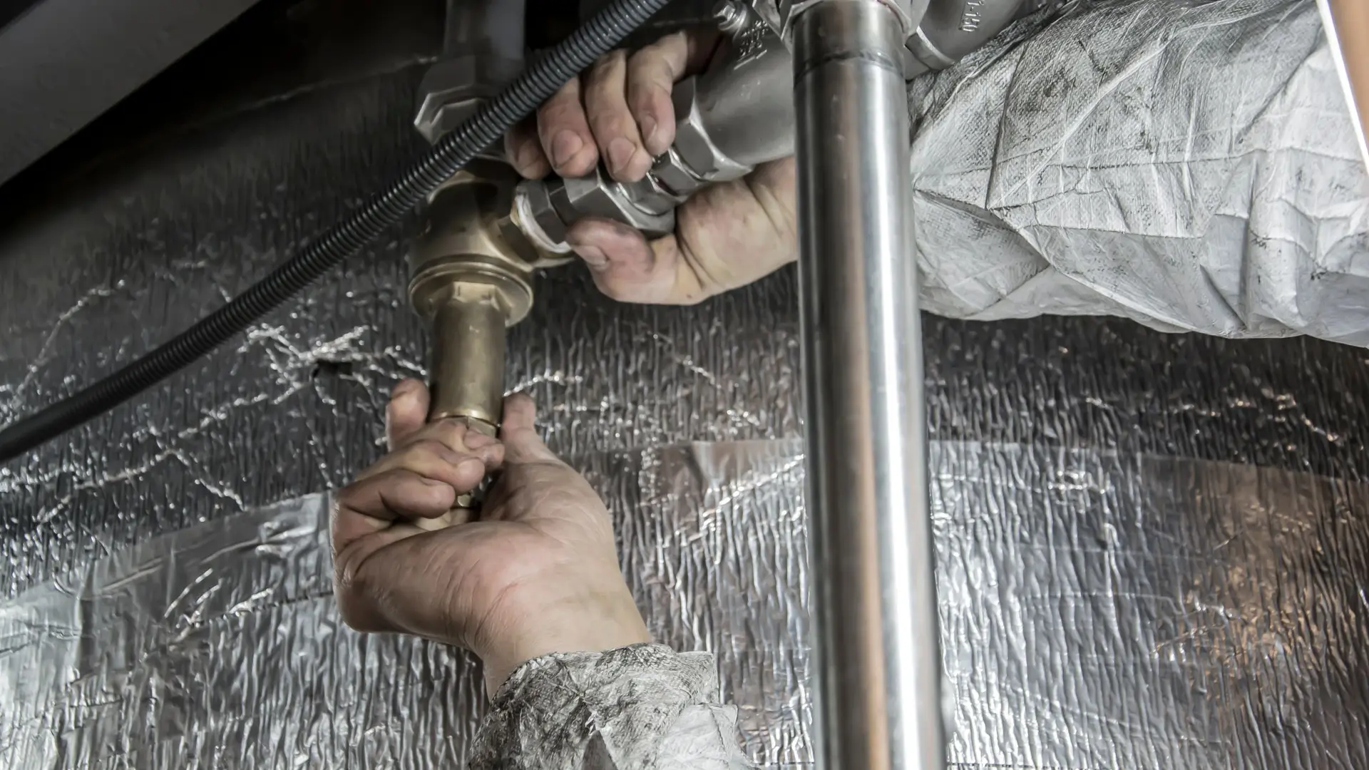 Plumber tightening a pipe fitting in a service void